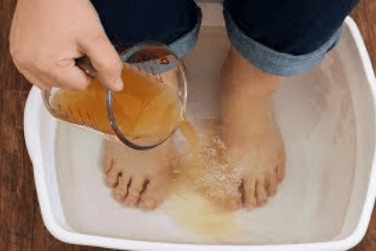 person soaking feet in a tub while pouring apple cider vinegar